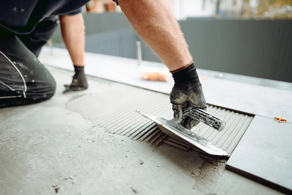 Ein Handwerker verlegt mit Werkzeug dunkle Bodenfliesen.