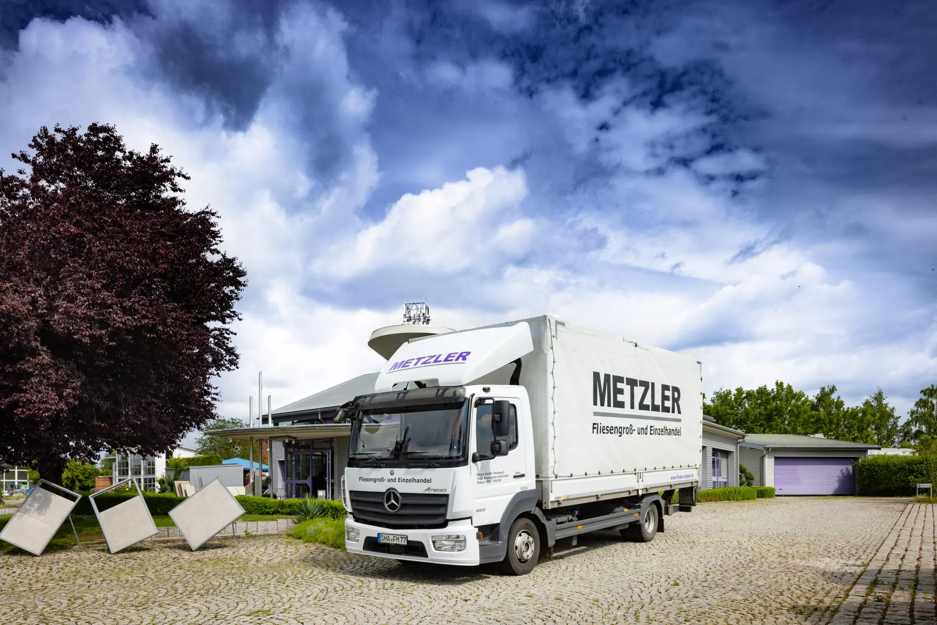 Ein großer Metzler-Lkw steht auf einem gepflasterten Hof vor dem Firmengebäude.