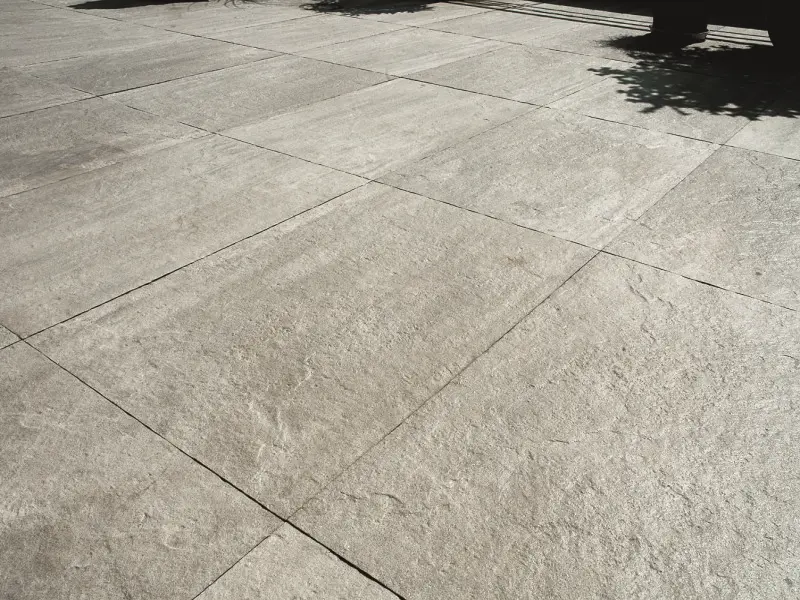 Graue, leicht strukturierte Außenfliesen werden von Sonnenlicht beschienen.