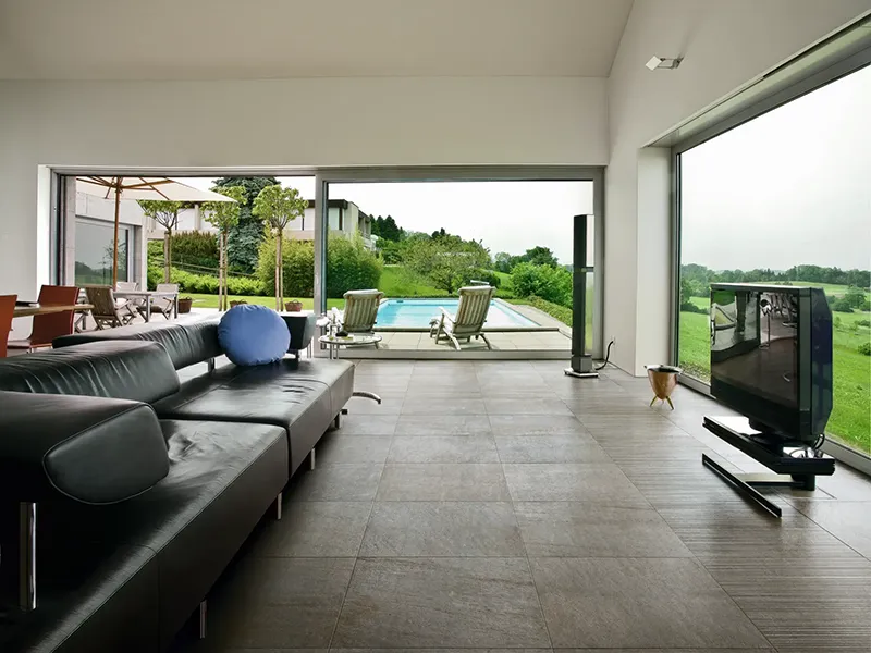 Das Wohnzimmer mit großen Glasfronten zeigt einen dunklen Fliesenboden und Blick auf den Pool.